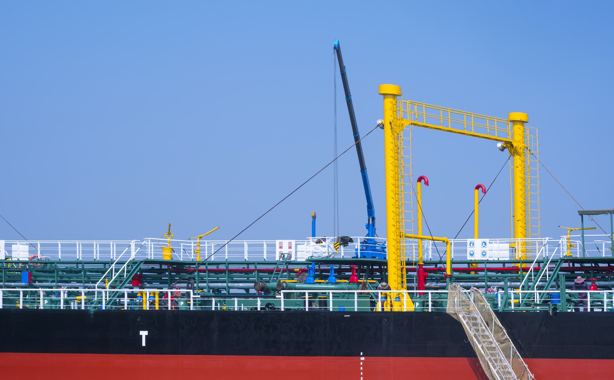 Oil pipeline system with crane machinery in tanker ship while moored at harbor against blue sky